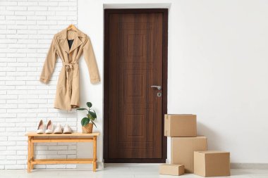 Koridorun içinde bir sürü paket, bankta ayakkabılar ve kapının yanında asılı palto var.