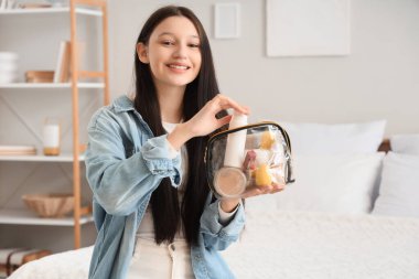 Kozmetik çantası ve makyaj malzemeleri olan genç kız yatak odasında.