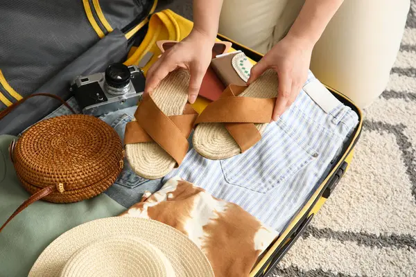 Otel odasında bavulunu elbiseleriyle açan genç bir kadın, yakın plan.