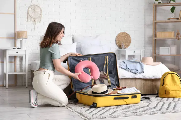 Güzel genç bir kadın, açık otel odasında bavulunu giysileriyle açıyor.