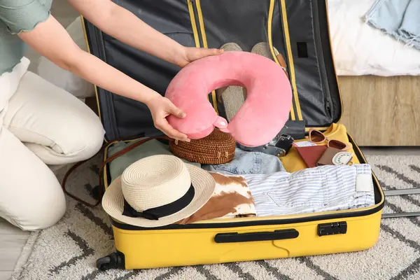 Genç bir kadın otel odasında bavulunu elbiseleriyle ve seyahat yastığıyla açıyor.