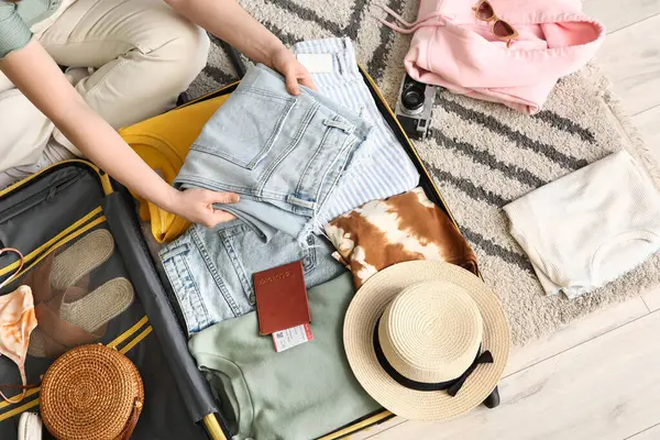 Otel odasında bavulunu elbiseleriyle ve pasaportuyla boşaltan genç bir kadın.