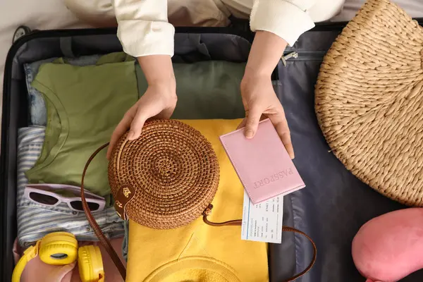 Genç bir kadın otel odasında bavulunu giysileri, pasaportu ve seyahat aksesuarlarıyla boşaltıyor.