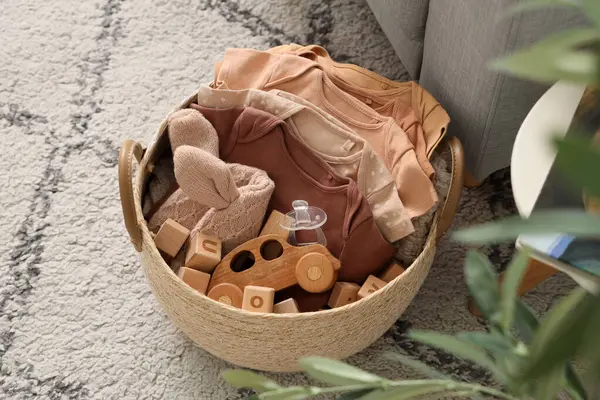 İçinde bebek kıyafetleri olan sepet ve odada halı üzerinde oyuncaklar.