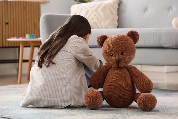 Otistik bozukluğu olan tatlı bir kız ve oyuncak ayı evde yerde oturuyor.