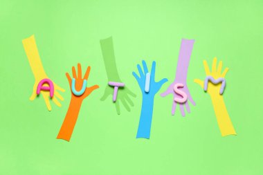 Yeşil arka planda plastikten yapılmış AUTISM sözcüğüyle kağıt eller