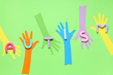 Yeşil arka planda plastikten yapılmış AUTISM sözcüğüyle kağıt eller