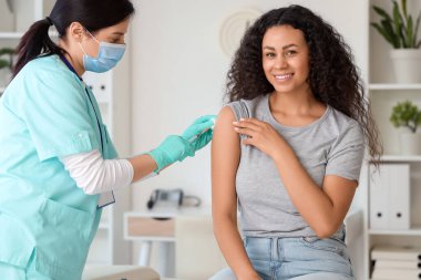 Kadın doktor klinikte Afro-Amerikan kadın aşılıyor.