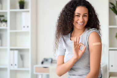 Uygulamalı tıbbi bandı olan genç Afro-Amerikalı kadın klinikteki aşıdan sonra iyi görünüyor.