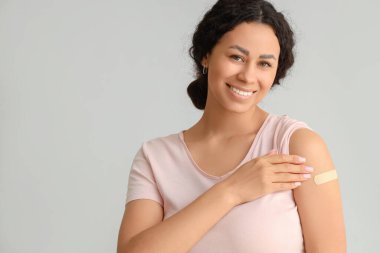 Hafif arka planda aşıdan sonra tıbbî yaması olan genç Afro-Amerikalı kadın, yakın plan.