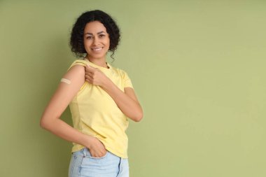 Yeşil arka planda aşıdan sonra tıbbi yaması olan genç bir Afro-Amerikalı kadın.