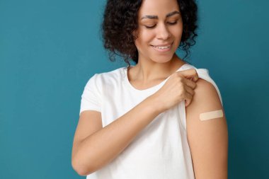 Mavi arka plandaki aşıdan sonra uygulamalı tıbbi yaması olan genç bir Afro-Amerikalı kadın.