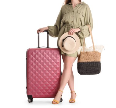 Beyaz arka planda yaz şapkalı, plaj çantalı ve valizli bir kadın turist.