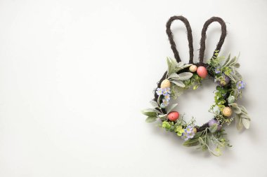 Güzel Paskalya çelengi boyalı yumurtalar ve çiçekler odadaki turkuaz duvarda asılı.