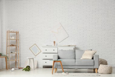 Gri kanepe, kahve masası ve deprem sonrası altüst olmuş çiçeklerle dolu dağınık bir oturma odası.