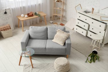 Gri kanepe, kahve masası ve deprem sonrası altüst olmuş çiçeklerle dolu dağınık bir oturma odası.