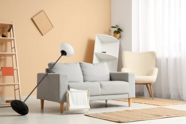 Gri kanepeli dağınık oturma odasının içi, standart lambayı ters çevirmiş ve depremden sonra rafları eğmiş.