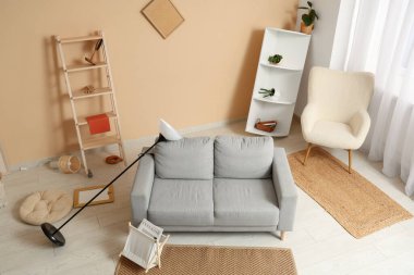 Gri kanepeli dağınık oturma odasının içi, standart lambayı ters çevirmiş ve depremden sonra rafları eğmiş.