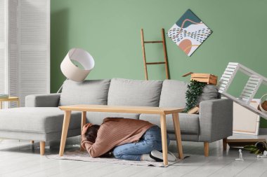 Deprem sırasında masanın altına saklanıp başını oturma odasına saklayan korkmuş genç bir kadın.