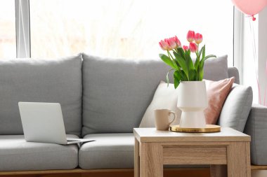 Kadınlar Günü için dekore edilmiş oturma odasındaki masada laleli vazo ve bir fincan çay.