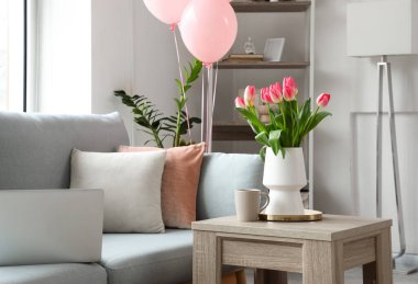 Kadınlar Günü için dekore edilmiş oturma odasındaki masada laleli vazo ve bir fincan çay.