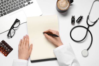 Kadın doktor elleri steteskop, dizüstü bilgisayar ve beyaz arka planda deftere bir fincan kahve yazıyor. Dünya Sağlık Günü