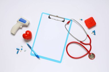 Beyaz arka planda steteskoplu boş bir pano, haplar ve kızılötesi termometre. Dünya Sağlık Günü