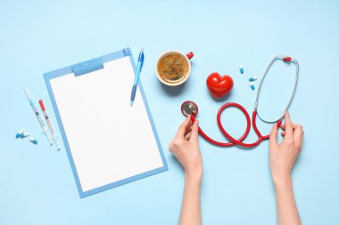 Steteskop, kırmızı kalp, bir fincan kahve ve mavi arka planda pano olan kadın elleri. Dünya Sağlık Günü