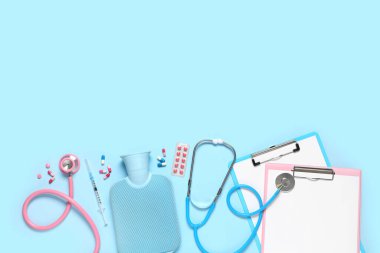 Stetoskoplu boş panolar, haplar ve mavi arka planda sıcak su şişesi. Dünya Sağlık Günü