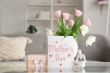 Anneler günü kartı. Oturma odasındaki masada çiçekler ve hediye kutusu var.