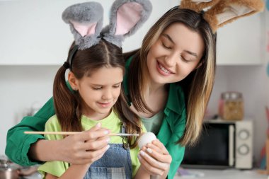 Küçük tatlı kızı tavşan kulaklarıyla mutlu bir anne. Bayram mutfağında paskalya yumurtası boyuyor.