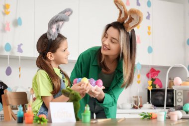 Mutlu anne ve küçük tatlı kızı tavşan kulakları ve bayram mutfağında boyalı Paskalya yumurtaları.