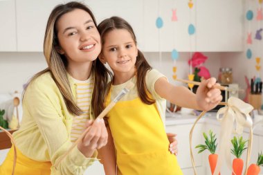 Mutlu anne ve sevimli küçük kızı neşeli mutfakta boyalı Paskalya yumurtaları için fırçalarla