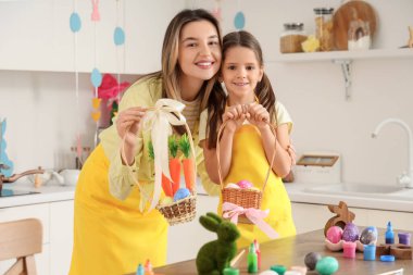 Mutlu anne ve küçük tatlı kızı ellerinde havuçlu boyanmış Paskalya yumurtası dolu sepetler tutuyorlar.