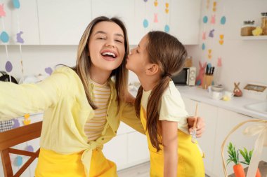 Mutlu anne ve boyalı Paskalya yumurtaları için fırçayla küçük tatlı kızı şenlikli mutfakta selfie çekiyorlar.