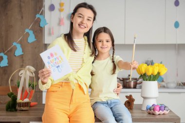Küçük tatlı kızının elinde tebrik kartı, fırça ve boyanmış Paskalya yumurtasıyla mutlu bir anne.