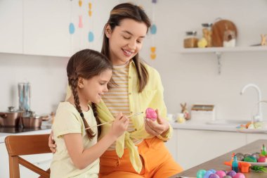 Mutlu anne ve küçük tatlı kızı neşeli mutfakta paskalya yumurtası boyuyor.