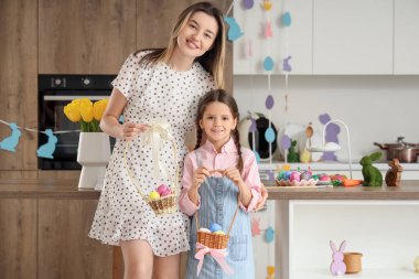 Mutlu anne ve küçük tatlı kızı neşeli mutfakta boyalı Paskalya yumurtaları taşıyorlar.