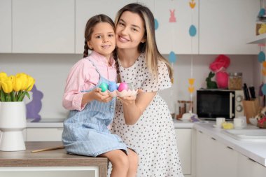 Mutlu anne ve küçük tatlı kızı neşeli mutfakta boyanmış Paskalya yumurtalarıyla