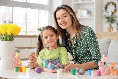 Mutlu anne, küçük tatlı kızıyla birlikte şenlikli oturma odasındaki masada paskalya yumurtası boyuyor.