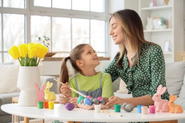 Mutlu anne, küçük tatlı kızıyla birlikte şenlikli oturma odasındaki masada paskalya yumurtası boyuyor.