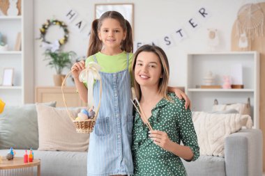 Mutlu bir anne, elinde fırça ve bir sepet boyalı Paskalya yumurtası tutan küçük tatlı kızıyla şenlikli oturma odasında.