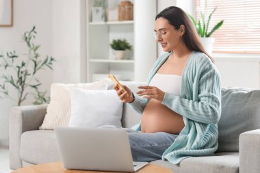 Evdeki koltukta cep telefonu kullanan hamile bir kadın.