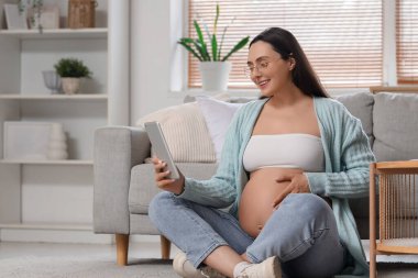 Evde tablet bilgisayar kullanan hamile bir kadın.