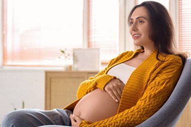 Evde sallanan sandalyede oturan genç hamile kadın