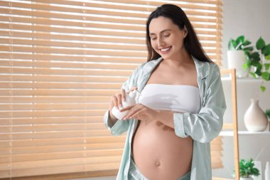 Genç hamile kadın banyoya krem sürüyor.