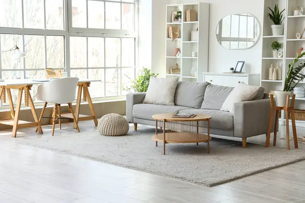Aydınlık oturma odasının içinde gri kanepe, işyeri ve ayna var.