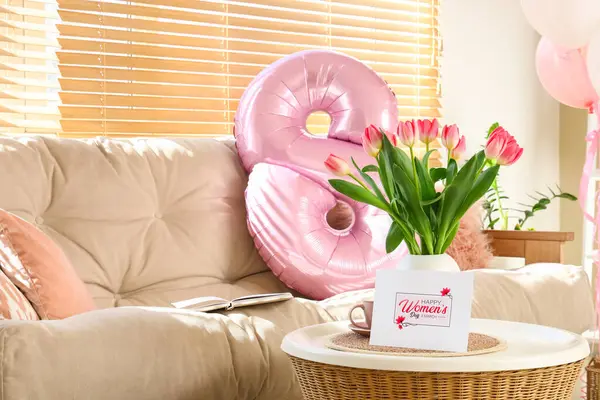 Vase with tulips and greeting card for Women's Day on table in living room