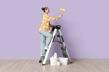 Leylak duvarının yanındaki merdivende boya silindirli genç bir kadın.