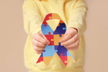 Otistik bozukluk ve bej arka planda farkındalık kurdelesi olan küçük çocuk, yakın plan.